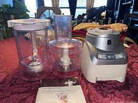 Three clear plastic attachments and base unit with manual on table.