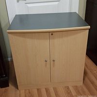 Storage cabinet angled view showing natural maple laminate sides and grey top.