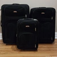 Front view of three black Delsey suitcases showing gradual size from small to large, all with front zippered compartments and brand logos.