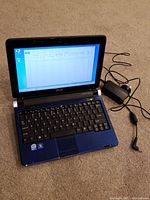Acer Aspire One netbook open with Windows 7 and Microsoft Word running, power adapter visible