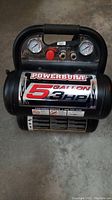 Front view of Powerbuilt air compressor showing gauges, control knobs and Powerbuilt 5 gallon 3HP label on tank.