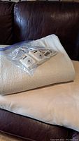 Full size electric blanket folded on leather couch with two wired Northern controllers in plastic bag on top.