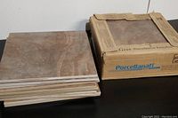 Stack of brown-beige textured ceramic tiles next to the original box, showing the tile surface and box branding with Porcellanati text.
