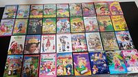 Front view of DVD cases neatly lined up, showing front covers of 30+ children's DVD titles including Dora the Explorer, Barbie, Disney Princess, and others.