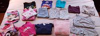 Photo showing assortment of children's clothing including sweaters, romper, leggings, jeans, tank tops and pajamas in size 14/16 spread on bed.