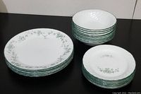 Grouped view showing stacks of 8 white dinner plates with green ivy pattern, 9 bread plates, and 10 bowls with swirl rim.