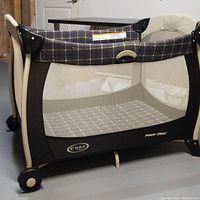 Side view of Euro Graco Pack 'N Play portable playard showing mesh sides, plaid fabric trim and wheels for mobility.