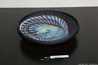 Top down view of glass bowl showing detailed blue and brown swirl pattern inside the bowl, with a Sharpie pen for size reference.