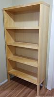Front view of one IKEA Agerum bookshelf showing four fixed shelves, natural birch veneer finish, standing on wooden floor.