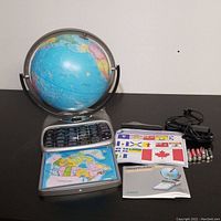 Oregon Scientific Smart Globe Deluxe Edition with globe, base, flag cards, manual, adapter, batteries, and stylus items laid out on a table.