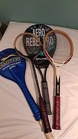 Four sports racquets are shown laid out on a surface: two wooden Slazenger tennis racquets, one Spalding racquet, and one black CRS racquet, along with a blue Slazenger racquet cover.