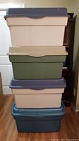 Stack of four storage bins showing colors and lids, two beige, one green, one blue.