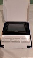 TomTom GPS device in open box showing the screen and part of packaging with support information.