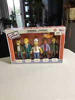 Original unopened box with five bendable The Simpsons figures lined up: Smithers, Mr. Burns, Homer, Carl, and Lenny. Box front reads Bendable, Poseable with bonus Blinky figure included.