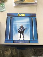 Front cover of AC/DC WHO MADE WHO vinyl LP showing blue background with guitar player figure and band logo.