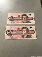 Two Canadian two dollar banknotes placed one above the other showing the front side with Queen Elizabeth II portrait and denomination 2 prominently displayed.
