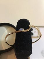 Full view of the gold filled opal bracelet displayed on a black cushion with a magnifying glass and smartphone nearby for scale and context.