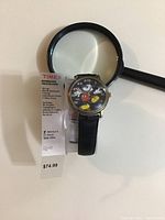 Wrist watch showing front face with Mickey Mouse character, black leather strap, and price tag.