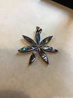 Top view of flower-shaped 925 sterling silver pendant with abalone shell inlays on seven petals displayed on a light surface.