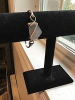 Photo of a handmade bracelet with a triangular rose quartz stone wrapped in sterling silver, displayed on a black bracelet stand near a window.