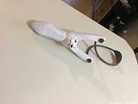 White wooden sling shot with black elastic band placed on a white surface, showing the full length and overall build.