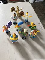 Front view of 9 colorful talking Simpsons figurines arranged on a white surface.