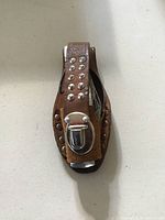 Front view of multi-tool secured in brown leather holder with metal studs and a silver clasp