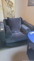 Front angled view of the velvet arm chair showing the seat cushion, back pillow, and one bolster pillow.