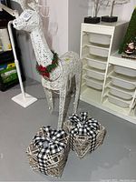 Full view of white light-up deer and two present box decorations on a gray floor indoors.