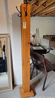 Full view of tall wood coat rack with square base and multiple metal hooks attached at different heights.