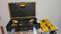 Black DeWalt tool case open containing two cordless tools and charger; five yellow DeWalt bit cases on table