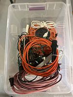 Top view of clear plastic bin containing various coiled extension cords and power bars, including an orange cable reel.