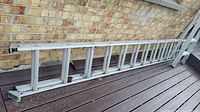 Side view of aluminum extendable ladder collapsed and resting against brick wall on wooden deck.
