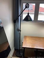 Full view of black adjustable floor lamp with pulley arm next to window and wooden table
