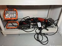 Photo showing all five power tools arranged on a white shelf, including the Power Light work light, heat gun, drill, grinder, and Skil saw with their cords