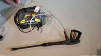 Front and side view of Ryobi electric pressure washer showing main unit with label, power cord, water hose, and pressure gun with lance attached.