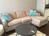 Front view of beige microfibre sectional sofa with chaise and teal throw pillows