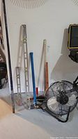 Photo of all items showing three levels, blue sledge hammer, clamp, and shop fan on floor against wall