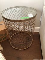 Front view of one side table showing cylindrical gold-tone metal lattice base and round clear glass top