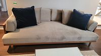 Front view of beige upholstered wooden frame sofa with two navy pillows on dark wood floor