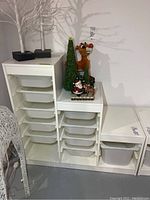 White storage cabinet with multiple translucent plastic bins inside cubby slots, placed in a basement setting with holiday decorations on top.