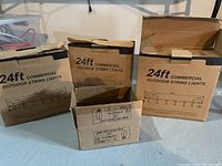 Three boxes of 24ft commercial outdoor string lights and one smaller box of LED bulbs placed on basement floor.