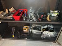 Two metal shelves with various hand tools, clamps, saws, drywall tools, and containers of screws and fasteners, plus paint rollers on bottom shelf.