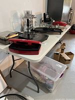 Side view of white plastic folding table holding various kitchen appliances.
