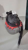 Front-top view of gray and red Husky wet/dry vacuum with hose attached, power cord wrapped around handle.