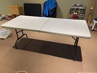 4 feet folding plastic table with metal legs shown fully set up in basement. Minor wear visible on surface.