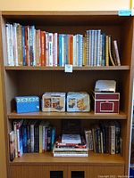 Full bookshelf showing a diverse collection of cookbooks, recipe card boxes in blue and red, and other books on shelves
