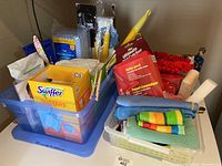 Plastic bins containing various cleaning supplies such as Swiffer dusters, microfiber pads, cleaning cloths, gloves, sponges.