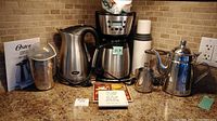 Photo showing the Black & Decker coffee maker with digital display, Oster electric kettle, T-Fal coffee grinder, stainless steel tea kettle, trivet, coaster, and other kitchen items on countertop.