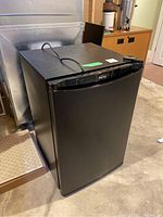 Matte black Danby bar fridge at an angle showing front and left side with power cord on top.